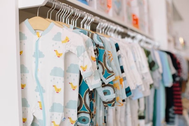 Soft cotton infant t-shirts and babywear on wooden hangers displayed in a bright nursery setup.