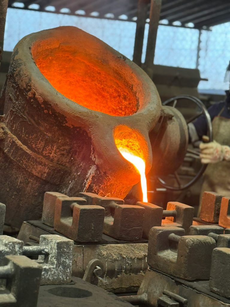 Molten metal pouring process inside an industrial foundry operated by casting manufacturers. This image shows molten metal being poured from a ladle into moulds during a controlled foundry operation. It represents the core production stage handled by casting manufacturers supplying engineered metal components for industrial and heavy-engineering applications. 